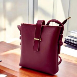 A small maroon purse rests elegantly on a wooden table, showcasing its vibrant color against the natural wood grain.